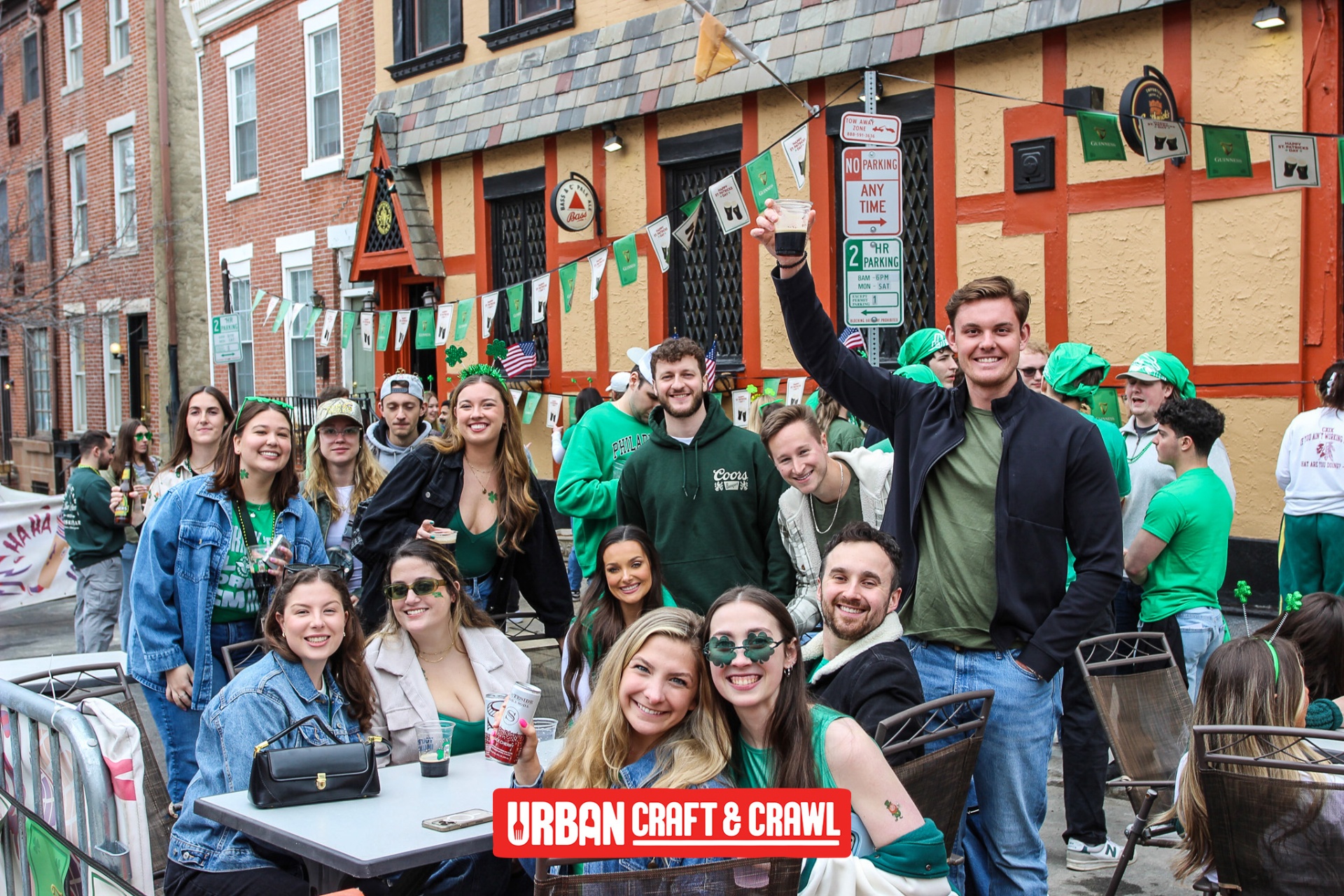 Group of friends in green celebrating outside a decorated Philadelphia pub during the Erin Express St Patrick's Day bar crawl